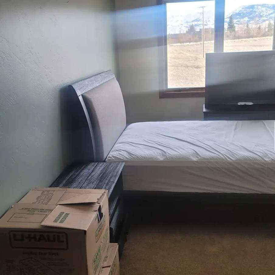 A room with a bed and a moving box on the floor provided by Dams Moving Company, a local moving company in Casper Wyoming.