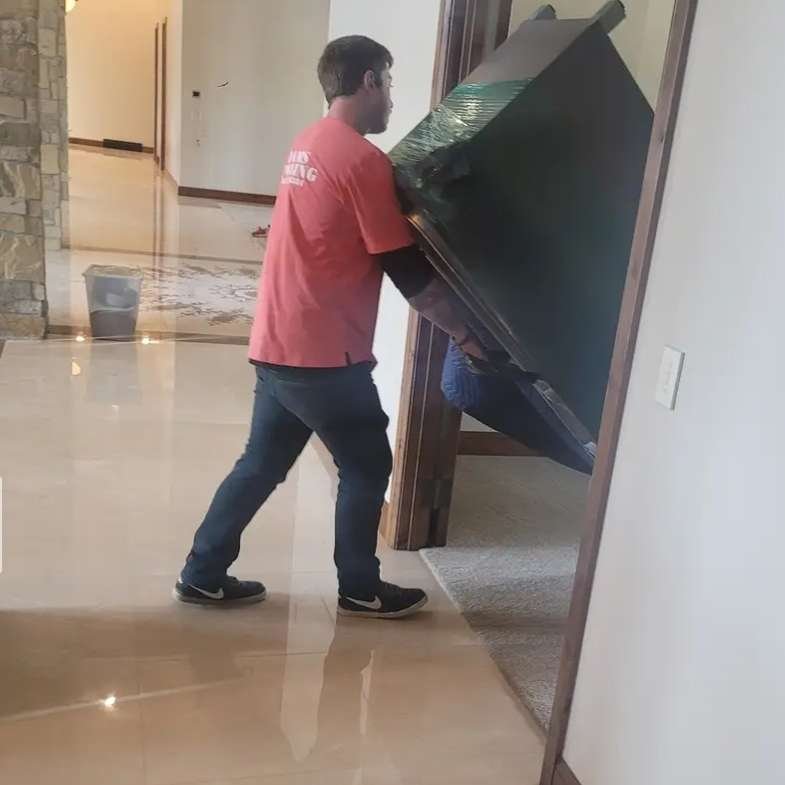 A moving helper from Dams Moving Company in Casper Wyoming assists a man with transporting a large box into a room.