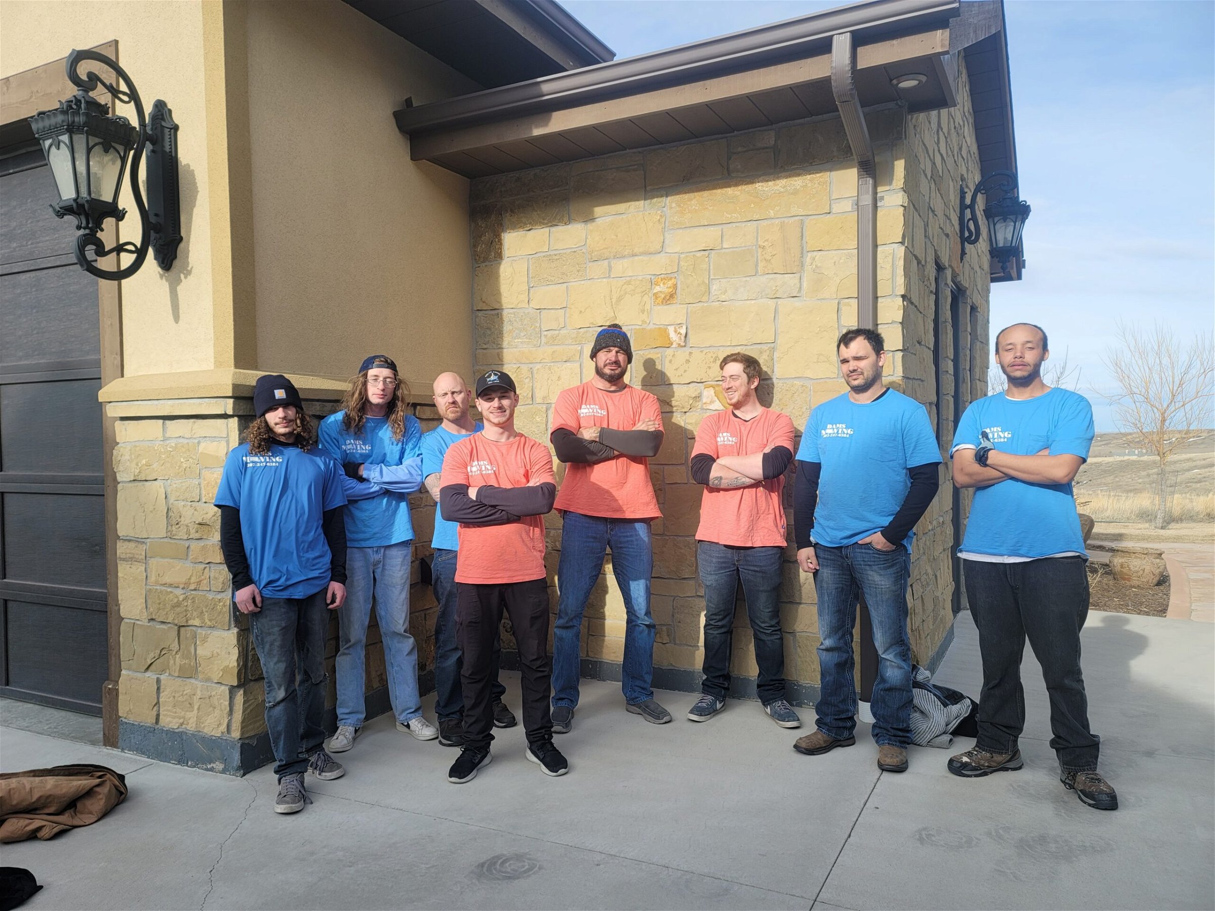 A group of people in blue shirts from Dams Moving Company in Casper Wyoming standing in front of a house, providing moving services.