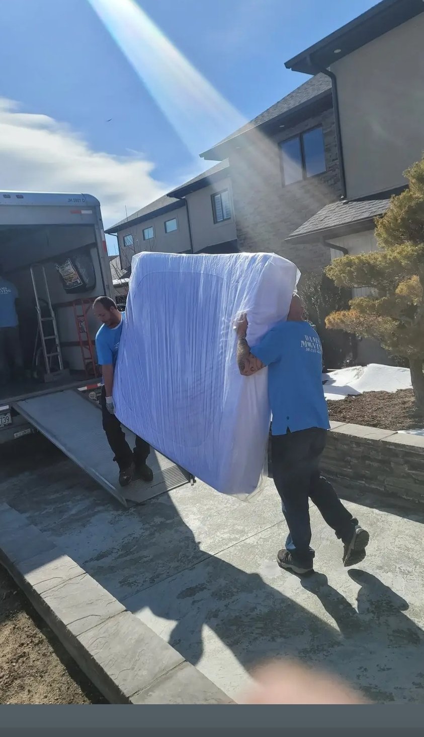 Two moving helpers transferring a mattress into a moving truck.