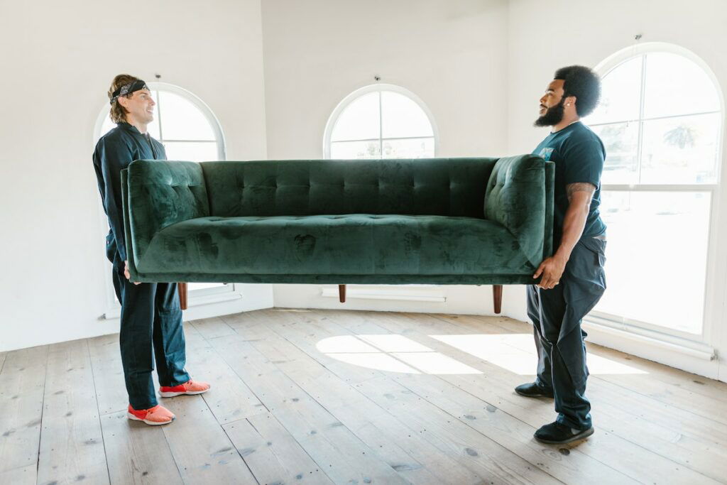 Two men carrying a green couch in a room while using Your Move techniques.