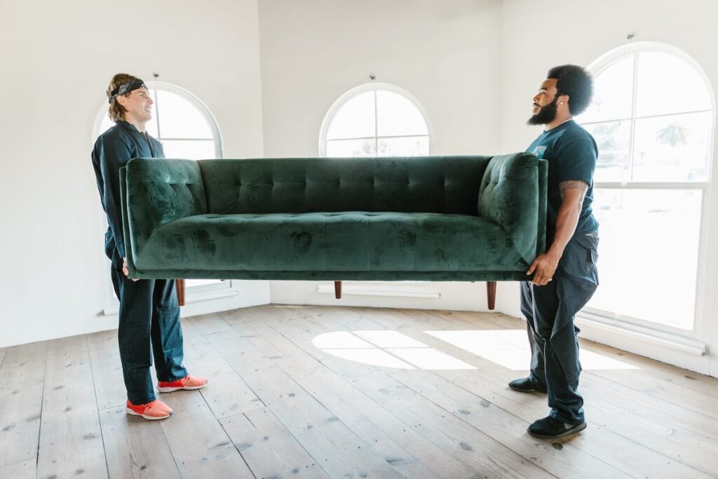 Two men efficiently transporting a green couch in a room.