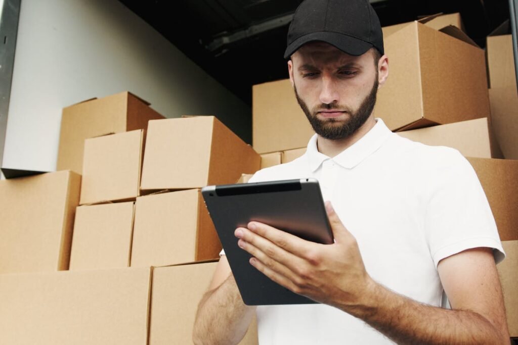 A man holding a tablet in front of boxes, showcasing the advantages of hiring packing professionals for a hassle-free move.