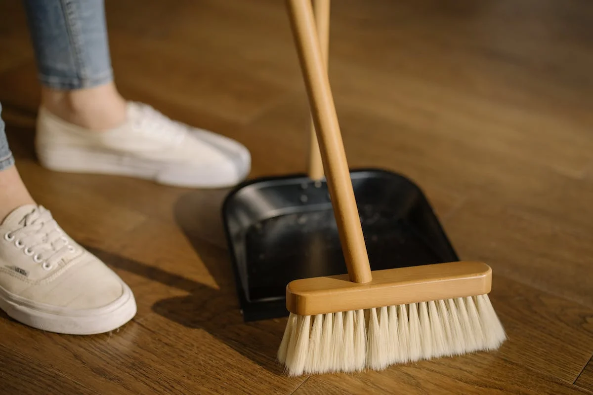 A woman with a broom next to a wooden floor, ensuring spotless spaces.