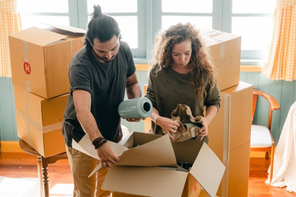 Hassle-Free Move - A man and woman hiring packing professionals to unpack boxes in a room.